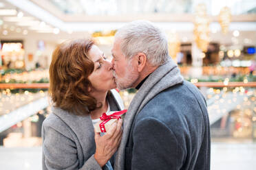 Senior couple doing Christmas shopping. A man giving a present to a woman. Shopping center at Christmas time. - HPIF29182