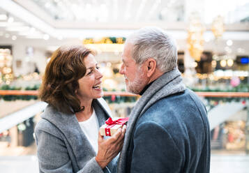 A senior man giving a present to a happy woman at shopping center at Christmas time. - HPIF29183