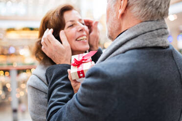 Ein älteres Ehepaar macht Weihnachtseinkäufe. Ein nicht erkennbarer Mann gibt einer Frau ein Geschenk. Einkaufszentrum zur Weihnachtszeit. - HPIF29184