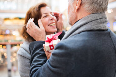 Senior couple doing Christmas shopping. An unrecognizable man giving a present to a woman. Shopping center at Christmas time. - HPIF29184