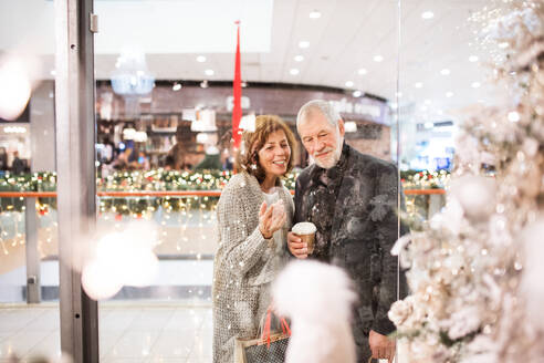 Senior couple doing Christmas shopping. Shopping center at Christmas time. Shot through glass. - HPIF29189