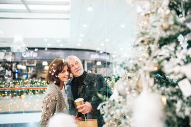 Älteres Ehepaar beim Weihnachtseinkauf. Einkaufszentrum zur Weihnachtszeit. Aufnahme durch Glas. - HPIF29190