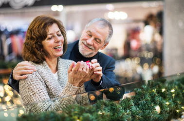 Ein Porträt eines älteren Paares, das ein eingepacktes Geschenk in einem Einkaufszentrum zur Weihnachtszeit hält. - HPIF29198