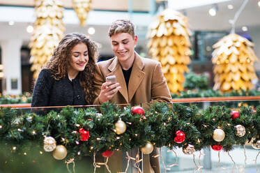 Ein glückliches junges Paar mit Smartphone in einem Einkaufszentrum zur Weihnachtszeit, Textnachrichten. - HPIF29213