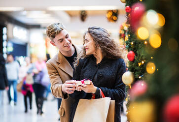 Ein glücklicher junger Mann, der seiner Freundin in einem Einkaufszentrum zur Weihnachtszeit ein Geschenk überreicht. Kopierraum. - HPIF29226