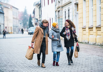 Großmutter und Enkelkinder im Teenageralter mit Papiertüten, die im Winter die Straße hinuntergehen. Konzept für Weihnachtseinkäufe. - HPIF29229