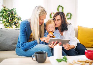 Ein Familientrio hält einen festlichen Moment auf einem Tablet fest und posiert für ein Selfie auf dem gemütlichen Sofa zu Hause - HPIF29236