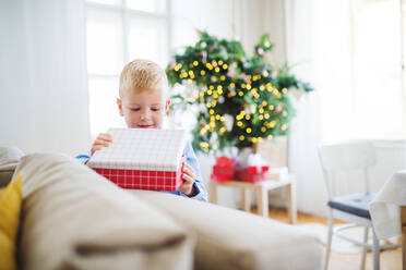 A small boy standing by a sofa at home at Christmas time, opening up a present. - HPIF29244