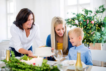 Ein kleiner Junge mit seiner Mutter, der die Großmutter betrachtet, die zu Hause zur Weihnachtszeit einen Kuchen auf den Tisch stellt. - HPIF29245