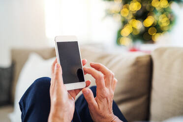 Nahaufnahme der Hände einer älteren Frau mit Smartphone zu Hause in der Weihnachtszeit, Kopierraum. - HPIF29256