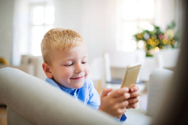 A small boy with smartphone sitting on an armchair at home at Christmas time, playing games. - HPIF29259