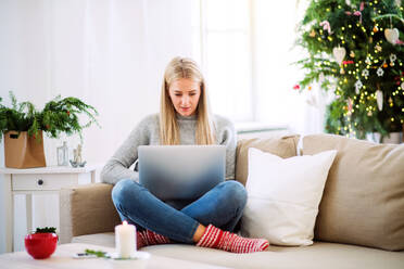 Eine junge Frau mit Laptop sitzt zur Weihnachtszeit zu Hause auf einem Sofa. - HPIF29261