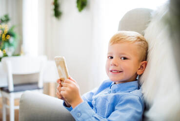 A small boy with smartphone sitting on an armchair at home at Christmas time, playing games. - HPIF29265