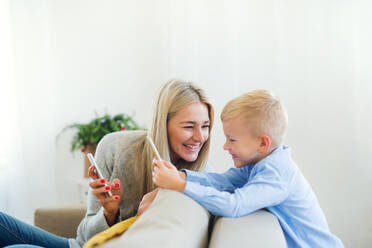 Eine Mutter und ein kleiner Junge mit Smartphones sitzen zur Weihnachtszeit zu Hause auf einem Sofa und spielen Spiele. - HPIF29270
