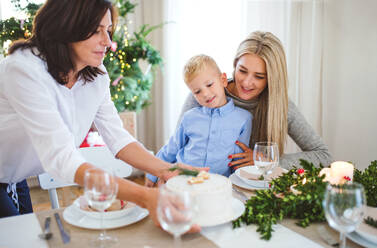 Ein kleiner Junge mit seiner Mutter, der die Großmutter betrachtet, die zu Hause zur Weihnachtszeit einen Kuchen auf den Tisch stellt. - HPIF29278