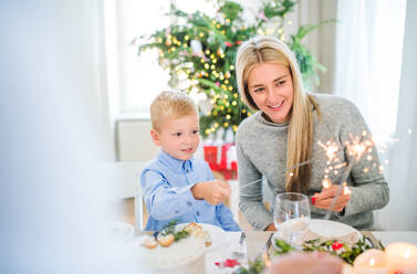 Ein kleiner Junge mit seiner Mutter sitzt zur Weihnachtszeit an einem Tisch und hält Glitzersteine in der Hand. - HPIF29283