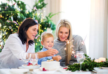 Ein kleiner Junge mit Mutter und Großmutter sitzt zur Weihnachtszeit an einem Tisch und hält Glitzersteine in der Hand. - HPIF29284
