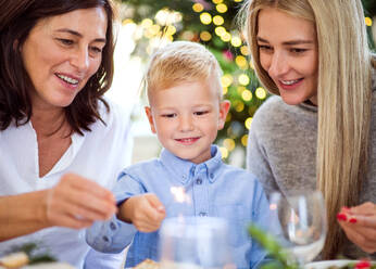 Ein kleiner Junge mit Mutter und Großmutter sitzt zur Weihnachtszeit an einem Tisch und hält Glitzersteine in der Hand. - HPIF29285