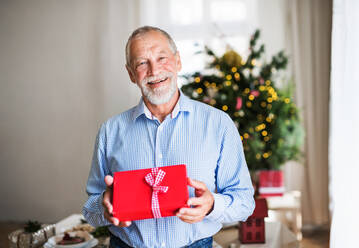 Ein Porträt eines älteren Mannes mit einem eingepackten Weihnachtsgeschenk. - HPIF29294