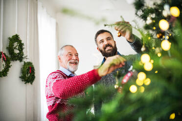 A happy senior father and adult son decorating a Christmas tree at home. - HPIF29336