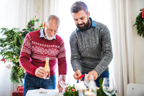 Ein älterer Vater und sein erwachsener Sohn decken einen Tisch für das Weihnachtsessen und unterhalten sich. - HPIF29338