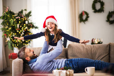 Ein kleines Mädchen mit Weihnachtsmannmütze spielt mit ihrem Vater zu Hause zur Weihnachtszeit und hat Spaß. - HPIF29350
