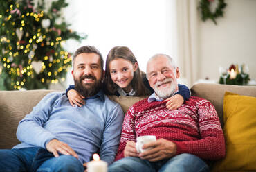 Ein glückliches kleines Mädchen und ihr Vater und Großvater sitzen zur Weihnachtszeit auf einem Sofa und posieren für das Foto. - HPIF29356