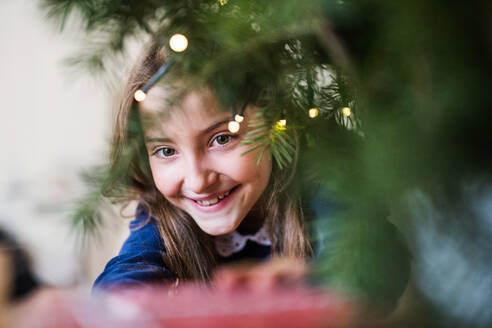 Nahaufnahme eines kleinen Mädchens, das zu Hause an einem Weihnachtsbaum steht. Raum kopieren. - HPIF29357