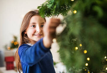 Ein kleines Mädchen, das zu Hause an einem Weihnachtsbaum steht. Platz kopieren. - HPIF29359