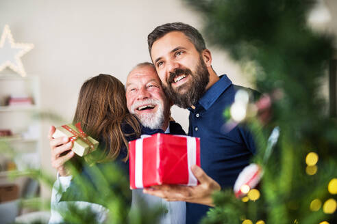 Ein kleines Mädchen mit Vater und Großvater, die zur Weihnachtszeit Geschenke austauschen und sich umarmen. - HPIF29364