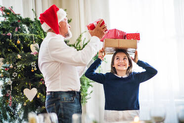 Ein älterer Mann mit einer Weihnachtsmannmütze und ein kleines Mädchen mit Geschenken auf dem Kopf zur Weihnachtszeit. - HPIF29375