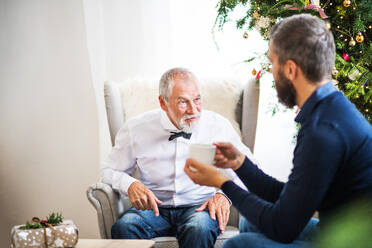 A senior father and adult son with a cup of coffee sitting on a sofa at Christmas time, talking. - HPIF29384