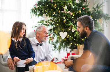 Ein kleines Mädchen mit seinem Vater und seinem Großvater, die zur Weihnachtszeit auf einem Sofa sitzen und sich unterhalten. - HPIF29386