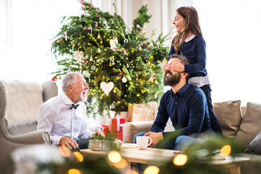 Ein kleines Mädchen mit Vater und Großvater sitzt zur Weihnachtszeit auf einem Sofa und hat Spaß. - HPIF29387