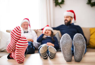 Ein kleines Mädchen mit Vater und Großvater sitzt zur Weihnachtszeit auf einem Sofa, die Füße auf einem Tisch und die Weihnachtsmannmützen auf dem Kopf. - HPIF29394