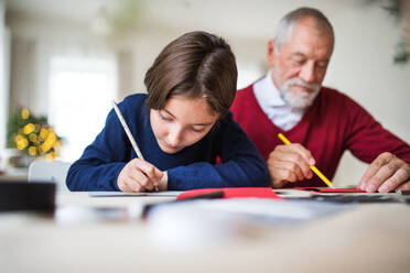 Ein kleines Mädchen und ihr Großvater sitzen an einem Tisch und schreiben gemeinsam Weihnachtskarten. - HPIF29398