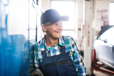 Eine ältere Frau steht mit verschränkten Armen in einer Werkstatt und repariert ein Auto. - HPIF29400