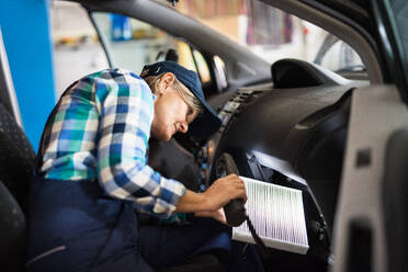 Eine ältere Frau arbeitet in einer Werkstatt und repariert ein Auto. - HPIF29409