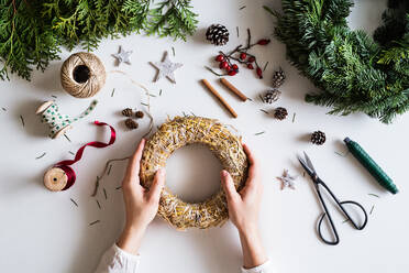Christmas composition on a white background. Flat lay. Female hands holding wreath from straw. - HPIF29412
