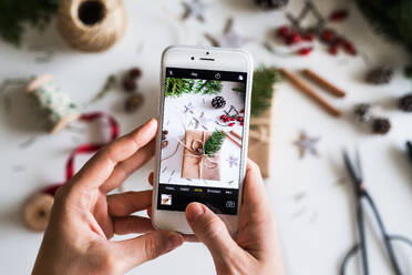 Christmas composition on a white background. Flat lay. Female hands holding a smartphone, taking a photograph. - HPIF29413