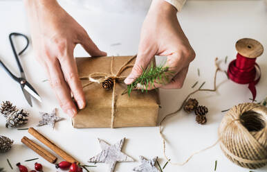 Weihnachtskomposition auf weißem Hintergrund. Weibliche Hände dekorieren ein eingepacktes Geschenk. - HPIF29414