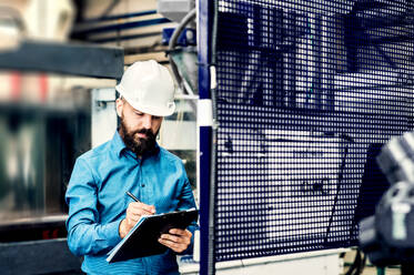 A portrait of a mature industrial man engineer with clipboard in a factory, working. Copy space. - HPIF29486