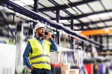 A portrait of a mature industrial man engineer with smartphone in a factory, making a phone call. - HPIF29492