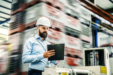 A portrait of a mature industrial man engineer with clipboard in a factory, working. Copy space. - HPIF29499