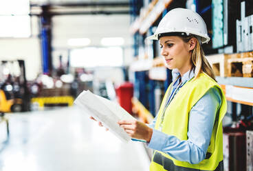 A portrait of a young industrial woman engineer in a factory holding paperwork, checking something. Copy space. - HPIF29505