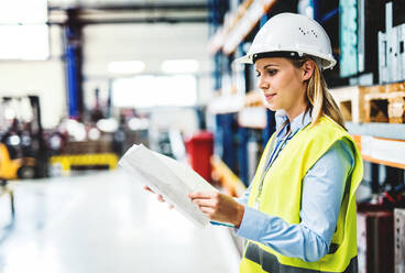 Das Porträt einer jungen Ingenieurin in einer Fabrik, die Papierkram in der Hand hält und etwas überprüft. - HPIF29505