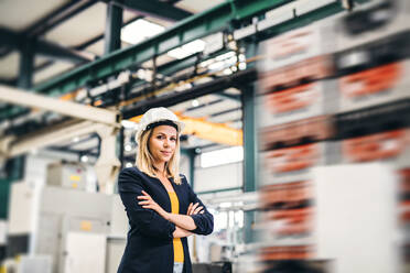 Das Porträt einer jungen Ingenieurin, die mit verschränkten Armen in einer Fabrik steht. - HPIF29508