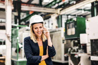 Das Porträt einer glücklichen Ingenieurin, die in einer Fabrik steht und telefoniert. - HPIF29512
