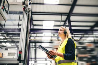 Porträt einer jungen Ingenieurin mit Headset und Klemmbrett in einer Fabrik bei der Arbeit. - HPIF29516