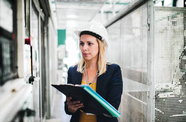 A portrait of a young industrial woman engineer in a factory, writing. - HPIF29527